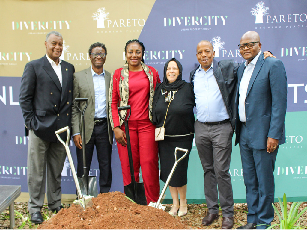 Six people stand together in business attire, posing for a photo in front of branded banners and a mound of soil with ceremonial spades at the Pareto Menlyn Park development. - Pareto Properties