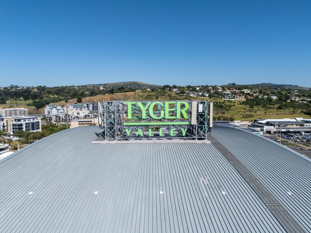 A large sign on a rooftop reads "Tyger Valley," with buildings, trees, and hills visible in the background under a clear blue sky, showcasing the vibrant area surrounding Tyger Valley Centre Bellville. - Pareto Properties