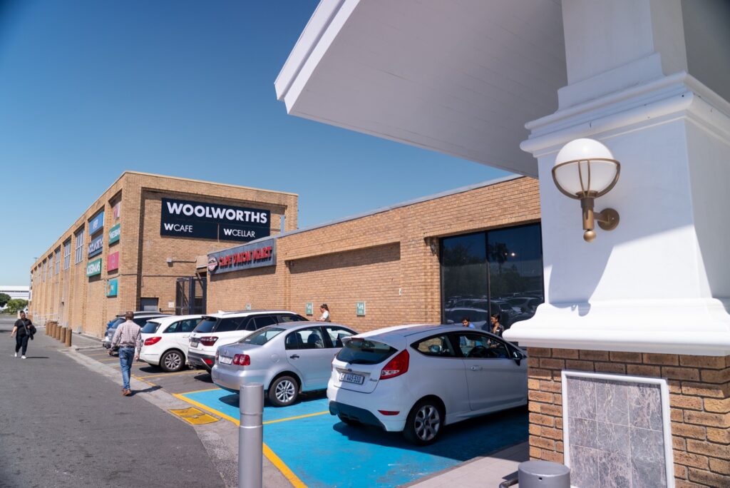 Car park outside a Woolworths supermarket at Tyger Valley Centre Bellville, with several parked cars and people walking near the entrance under a clear blue sky. - Pareto Properties
