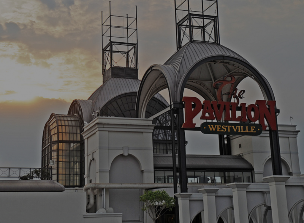 Exterior view of The Pavilion shopping centre in Westville, featuring large arches, glass roofing, and a prominent red and yellow sign at sunset. - Pareto Properties