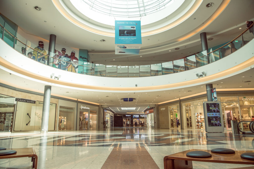 Interior of a modern shopping centre with empty walkways, shopfronts on both levels, and a large skylight above letting in natural light. - Pareto Properties