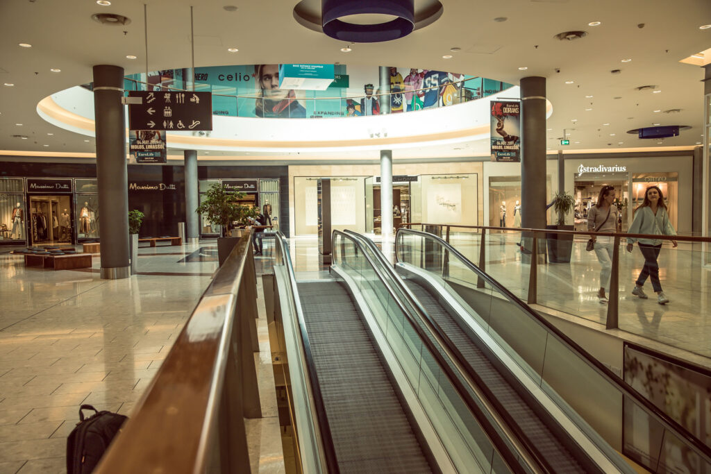 Interior of a shopping centre with an empty escalator, shiny tiled floors, visible shopfronts, and a few people walking in the background. - Pareto Properties