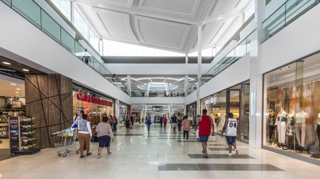 Interior view of a modern shopping centre with people walking, shops on both sides, and a bright, spacious atrium. - Pareto Properties