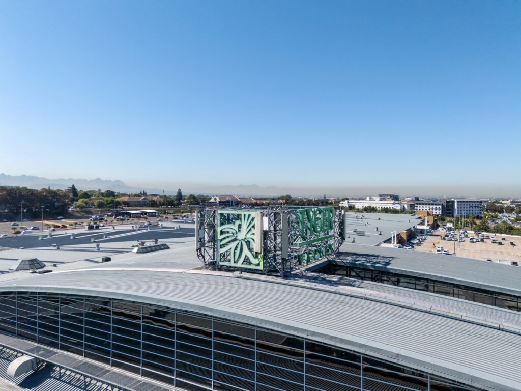 A large rooftop air conditioning unit with green and white panels sits atop a modern industrial building, typical of those found in Pareto portfolio shopping centres, under a clear blue sky. - Pareto Properties
